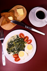 Healthy breakfast. Fresh boiled eggs with cherry tomatoes and spinach in cheese sauce. Coffee and buttered toast. Proper nutrition.