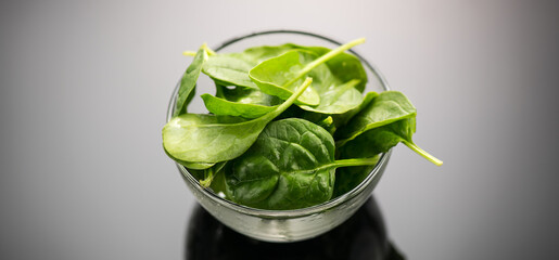 Spinach in a transparent glass bowl on gray background with reflection. Heap of Baby spinach fresh...
