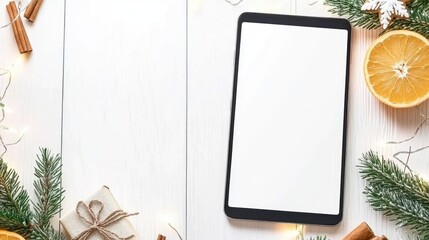 A festive Christmas scene featuring a black tablet, decorated orange slices, gingerbread, and lights on a white wooden table