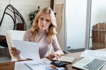 Focused Caucasian business woman looking through paper documents, managing business affairs,...