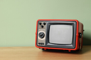Obraz premium Retro tv set on wooden shelf against green wall. Space for text