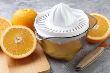 Plastic juicer, oranges and knife on grey table, closeup