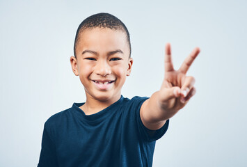 Boy, portrait and peace sign in studio, child and proud of symbol for kindness on white background....