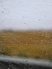 Raindrops on glass window with soft yellow bokeh background. Abstract nature composition with water droplets creating warm, sunny atmosphere. Perfect for wellness, mindfulness, and optimistic 