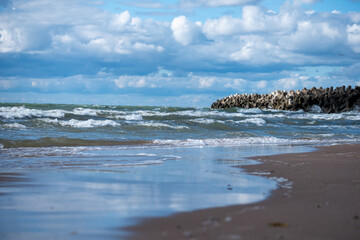 Waves gently roll onto the sandy shore beneath a sky filled with clouds at a scenic coastal...