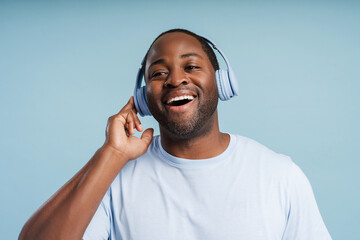 Happy African American man wearing wireless headphones listening to music in studio