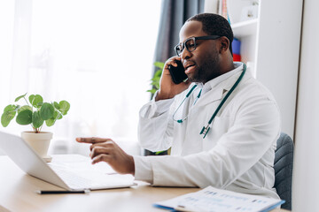 African American doctor working with laptop talking on the smartphone in clinic