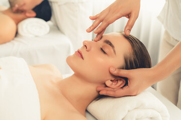 Caucasian couple enjoying relaxing anti-stress head massage and pampering facial beauty skin recreation leisure in dayspa modern light ambient at luxury resort or hotel spa salon. Quiescent