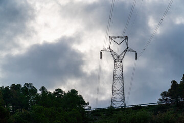 High voltage tower on top of a hill, cloudy sky in the background.