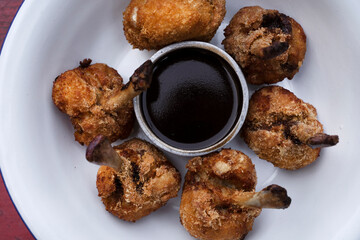 Top view of deep fried breaded chicken wings with a bittersweet dipping sauce, in a white bowl on the red wooden table.