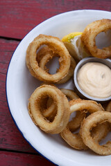 Deep fried seafood. Top view of delicious fried squid rings with lemon and a dipping sauce in a white bowl.	
