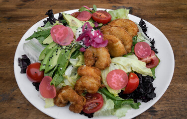 Gourmet salad. Top view of a fresh sea salad with lettuce, cherry tomatoes, avocado, radish and onion pickles, seeds and cream cheese, in a white dish on the wooden table.