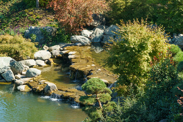 Cascade waterfall on the large lake Oike in Japanese garden. Public landscape park of Krasnodar or Galitsky Park, Russia.