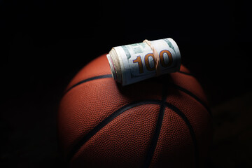 Rolled hundred dollar bill on a basketball,  on black background