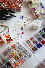 Hand figurine, colorful friendship bracelets, necklaces, various beads and DIY supplies on the table. Making jewelry at home. Selective focus.