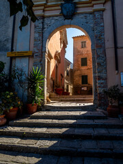 Fototapeta premium Torbogen in der historischen Altstadt von Marciana, Elba, mit Sonnenstrahlen, die durch den Bogen scheinen – Mediterraner Charme und antike Architektur