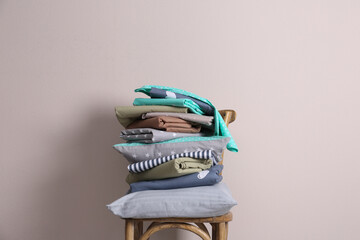 Stack of clean bed sheets and pillow on chair near beige wall