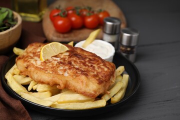 Tasty soda water battered fish, lemon slice and potato chips on dark wooden table