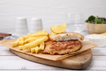 Tasty soda water battered fish, potato chips and lemon slice on white wooden table