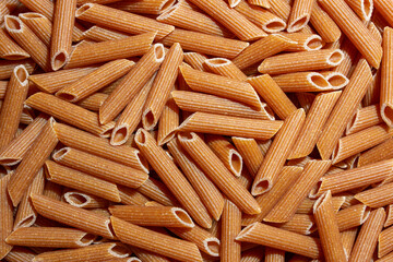 Uncooked Whole Grain Penne Rigate Pasta: A Culinary Canvas of Whole Wheat Macaroni, Creating a Lively and Textured Background for Gourmet Cooking. Whole Grain Dry Pasta. Whole Wheat Raw Macaroni