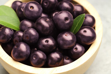 Ripe acai berries and leaves in bowl on table, closeup
