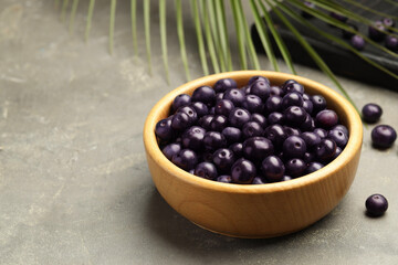 Ripe acai berries in bowl on grey textured table. Space for text