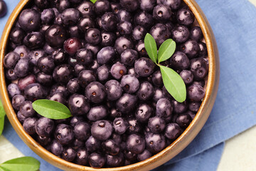 Ripe acai berries and leaves in bowl on table, top view