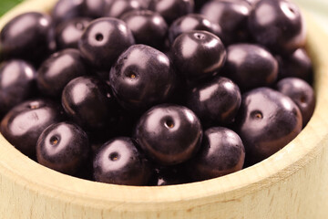 Ripe acai berries in wooden bowl, closeup