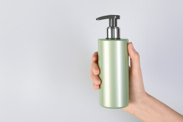 Woman with shampoo bottle on grey background, closeup. Space for text