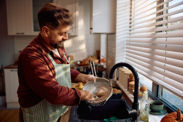 Smiling man washing dishes while cooking in kitchen.