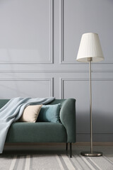 Comfortable sofa and lamp near grey wall in room