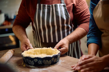 Close up of man making pie with his wife in  kitchen.