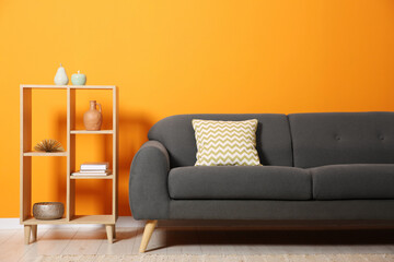 Stylish sofa with cushion and decor elements near orange wall
