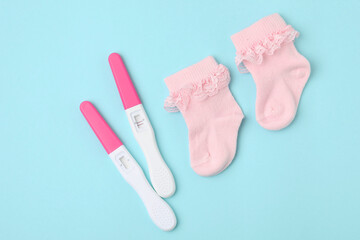 Pregnancy tests and pink socks on light blue background, top view