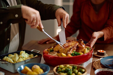 Close up of man carving Thanksgiving turkey at dining table.