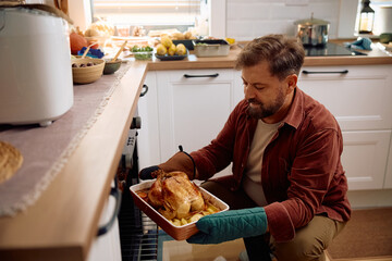 Happy man turkey in oven while roasting it for Thanksgiving dinner in  kitchen.