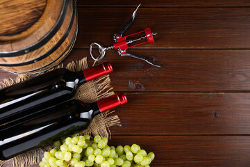 Obraz premium Wing corkscrew, bottles of wine, grapes and barrel on wooden table, top view. Space for text