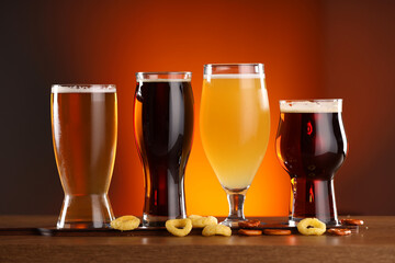 Glasses with different types of beer on wooden table against color background