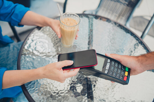 Fototapeta Cropped photo of two people hands hold smart phone terminal pay coffee street cafe table outdoors