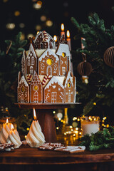 Christmas and New Year beautiful elegant family dinner table setting decorated with candles, fir tree branches, handmade craft toys. Gorgeous big homemade cake with gingerbread houses as centrepiece.