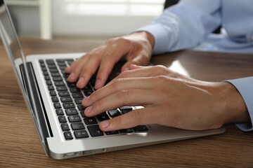 Businessman using laptop at wooden table, closeup. Modern technology