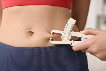 Doctor measuring woman's body fat with caliper in clinic, closeup