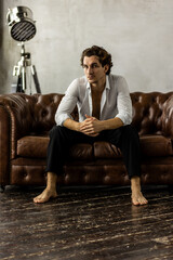 Portrait of a handsome young stylish sexy man in a white shirt, jeans jacket posing in studio with a loft interior. Black and white. Casual clothes, modern style