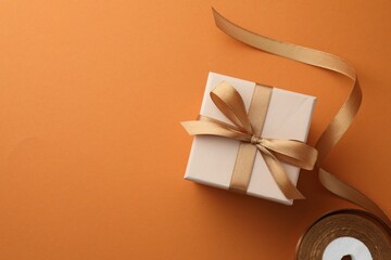 Beautiful gift box with golden bow and ribbon on orange background, top view. Space for text