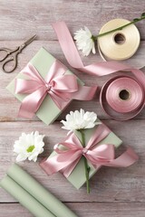 Gift boxes with bows, ribbon, scissors and flowers on pink wooden table, flat lay