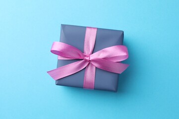 Gift box with bow on light blue background, top view