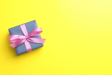 Gift box with pink bow on yellow background, top view. Space for text
