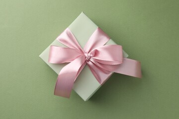 Gift box with pink bow on green background, top view