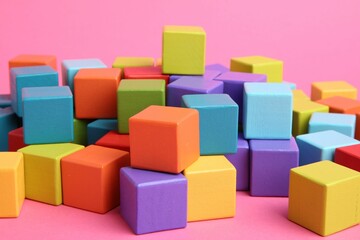 Many wooden colorful cubes on pink background, closeup
