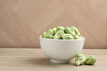 Fresh green Brussels sprouts in bowl on wooden table, space for text